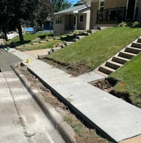 New concrete sidewalk along a sloped residential street beside a house and stairs