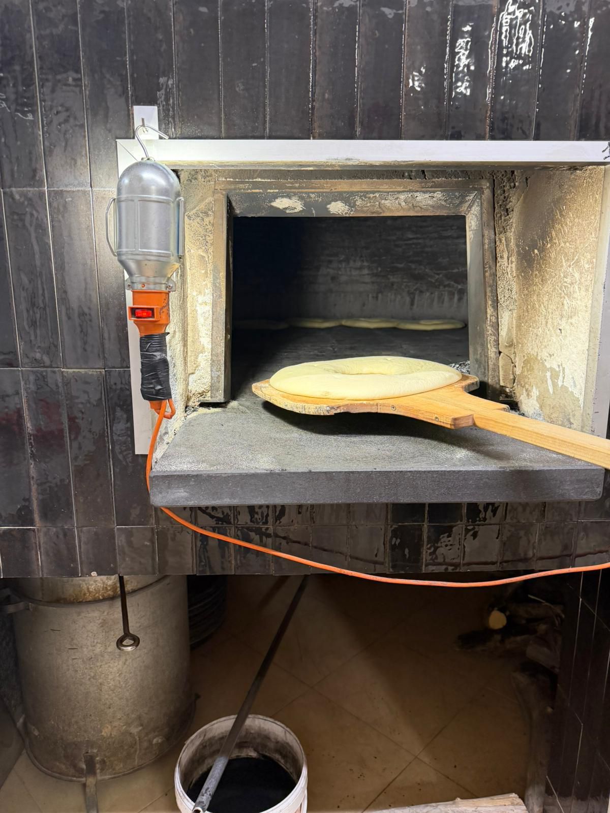 Pane piatto cotto in un forno di pietra con una pala di legno. Forno di mattoni grigi in cucina.
