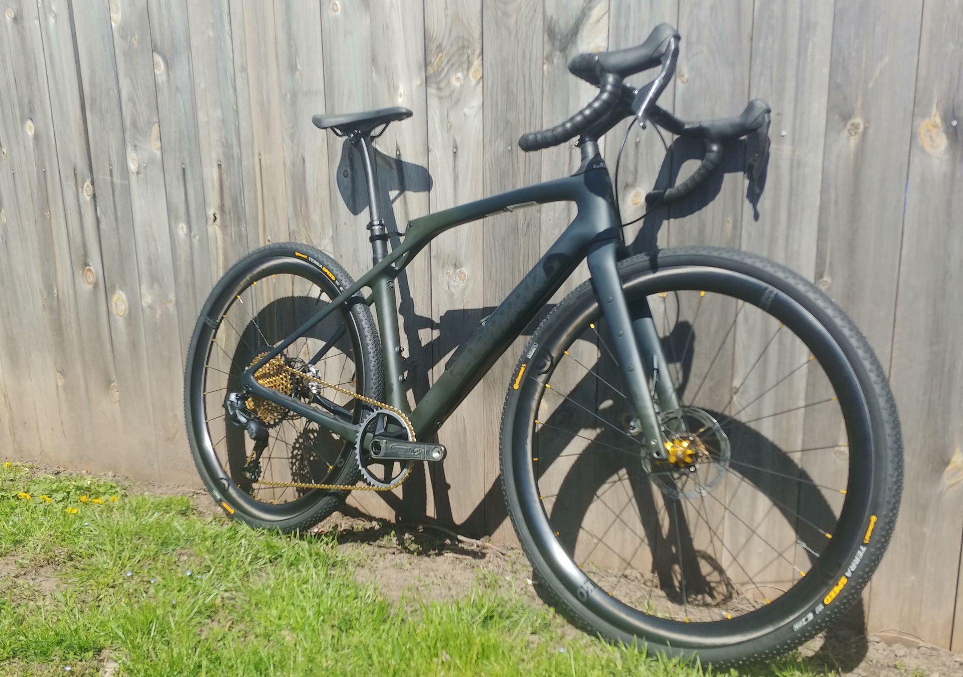 Black road bike with aero bars parked on grass in front of a wooden fence