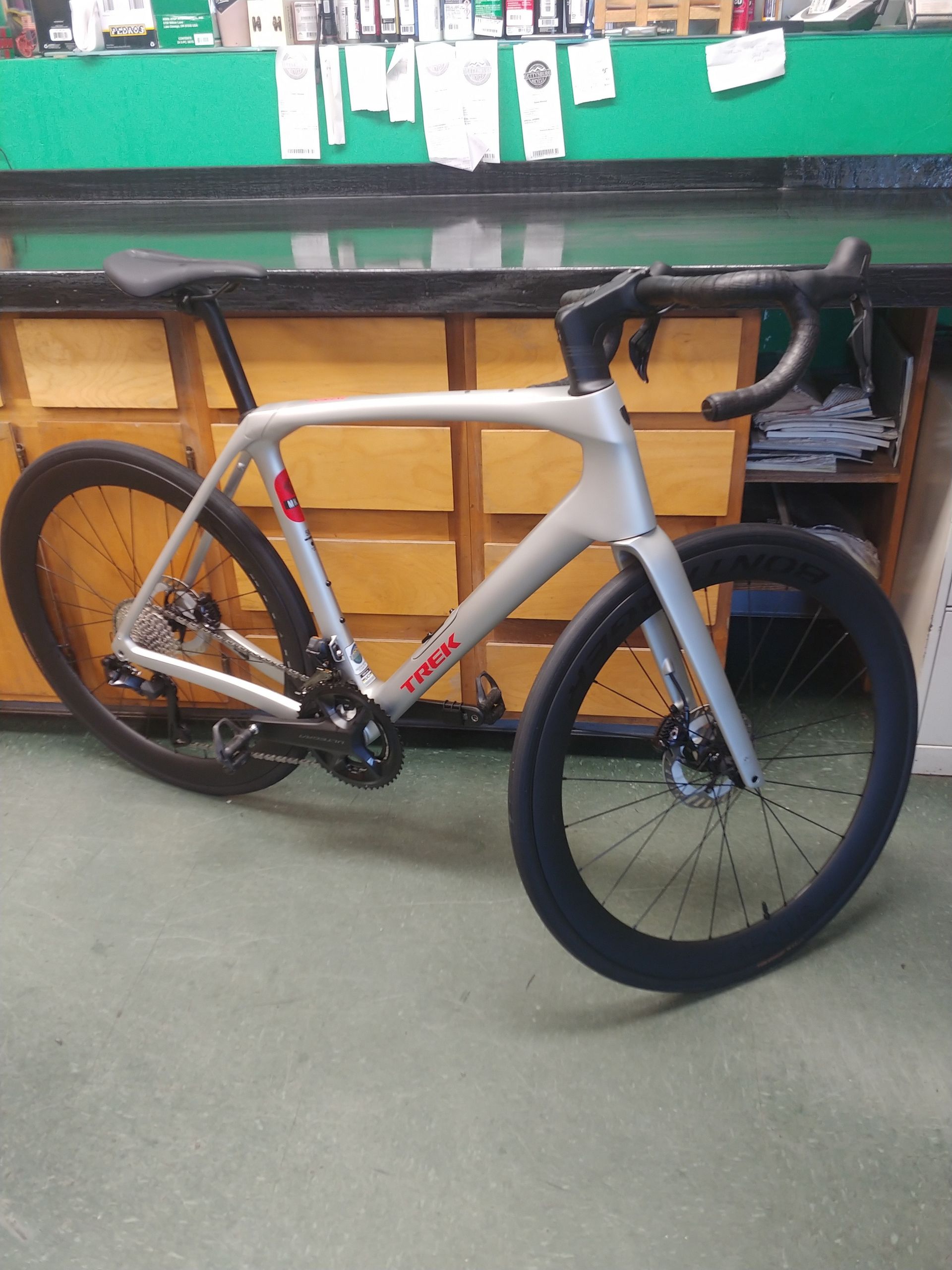 Gray road bike with deep-section black front wheel and drop handlebars in a workshop against a workbench.