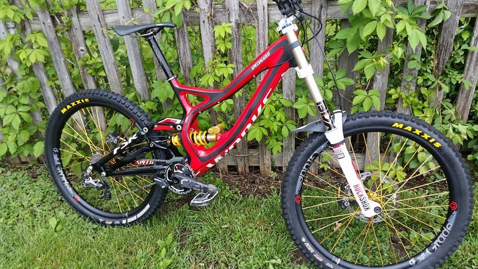 Red full-suspension mountain bike with white front fork and yellow-rimmed wheels on grass by a wooden fence