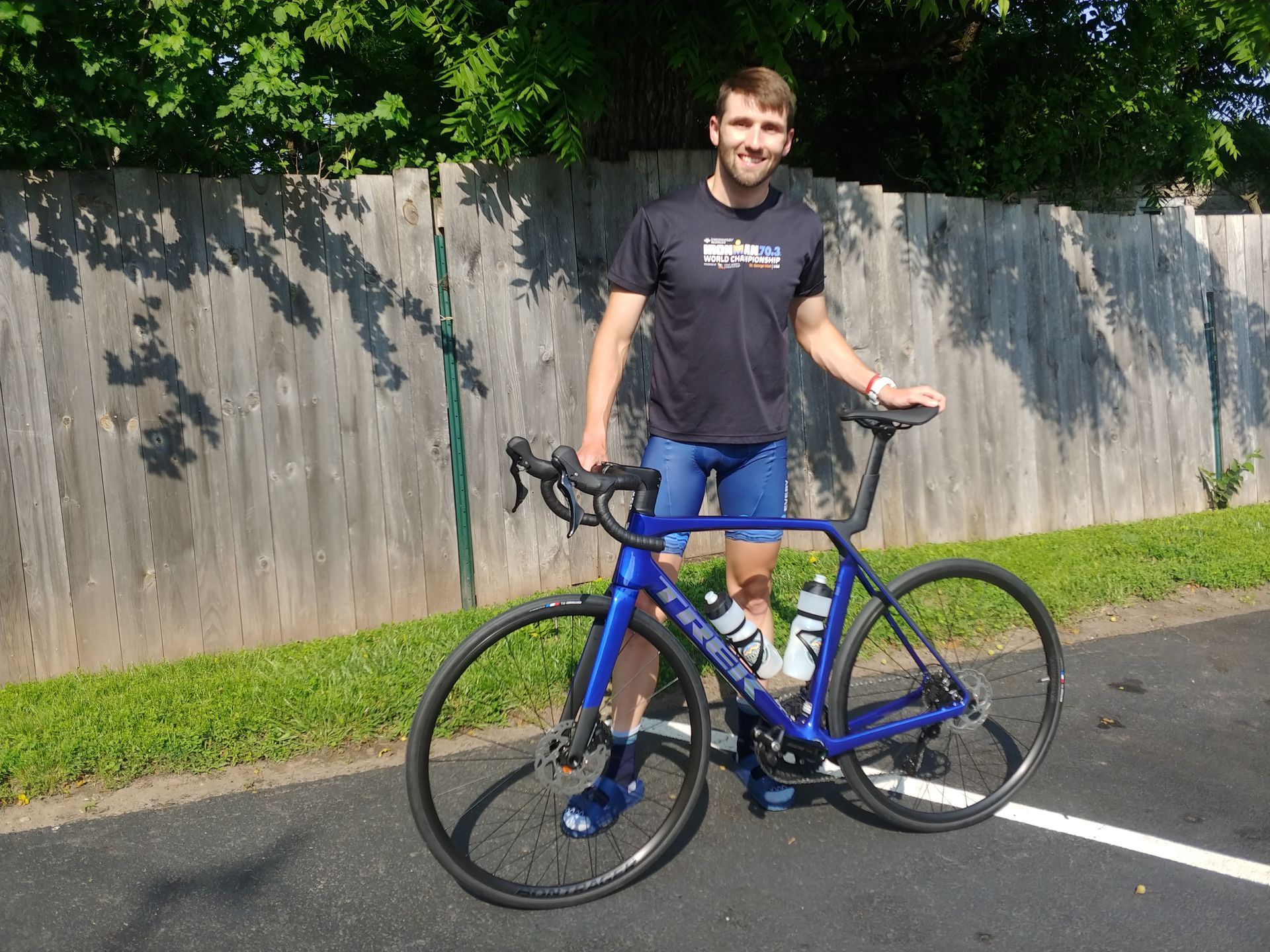 Person standing beside a blue road bike in a parking lot, smiling at the camera.