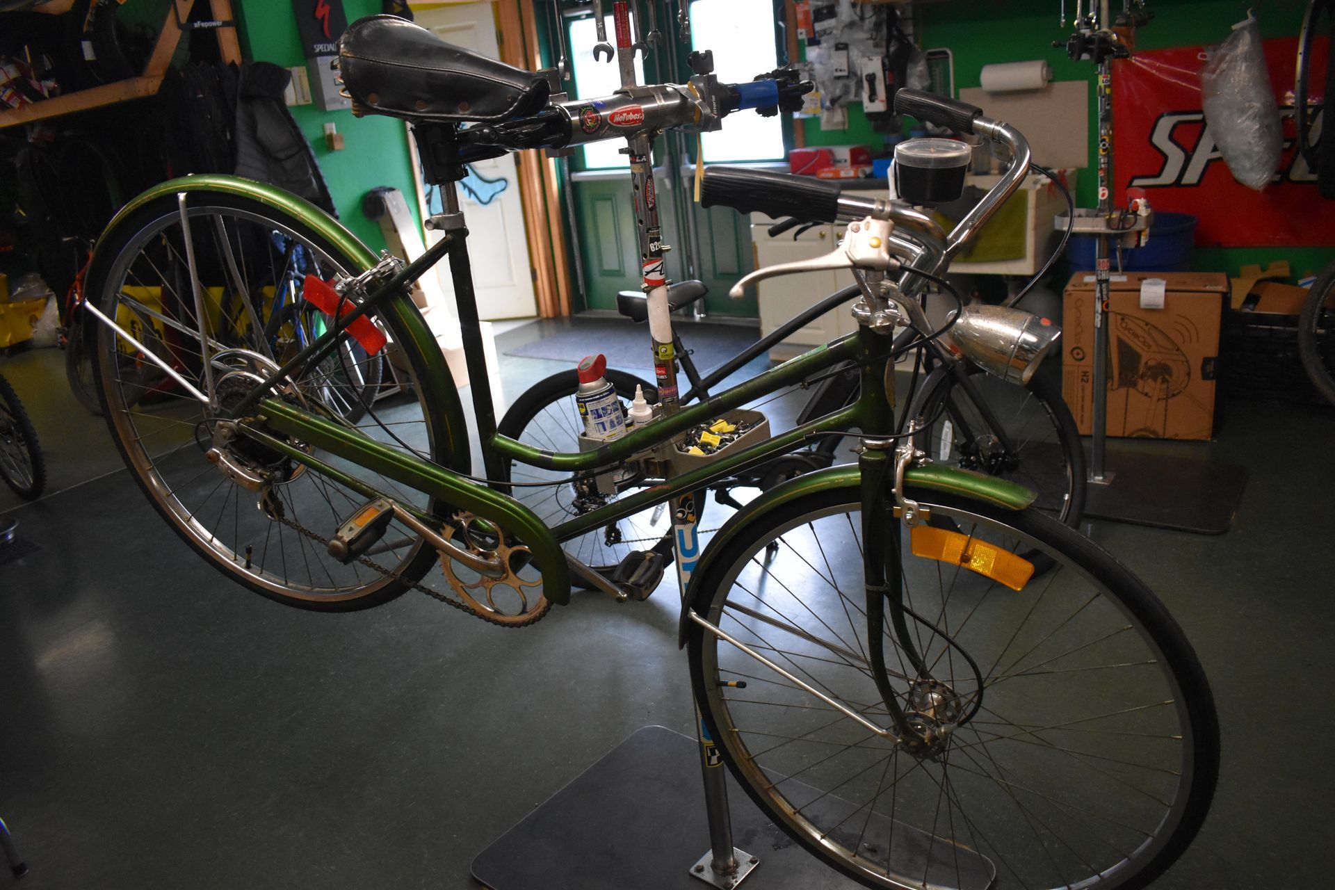 Two bicycles parked indoors in a garage, one silver and one green, near tools and shelves.