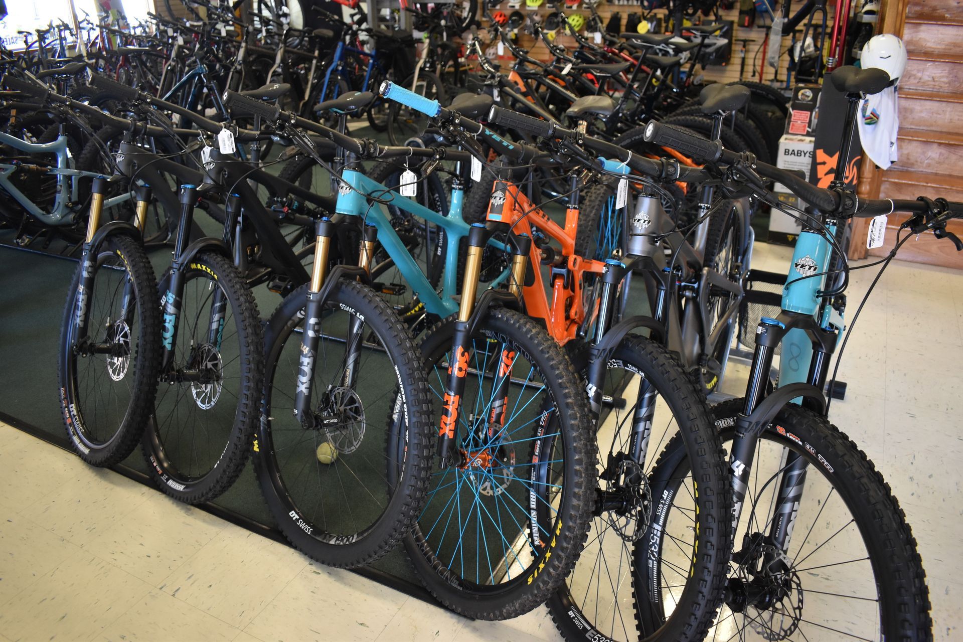 Rows of mountain bikes parked indoors, including blue and orange bikes in the foreground