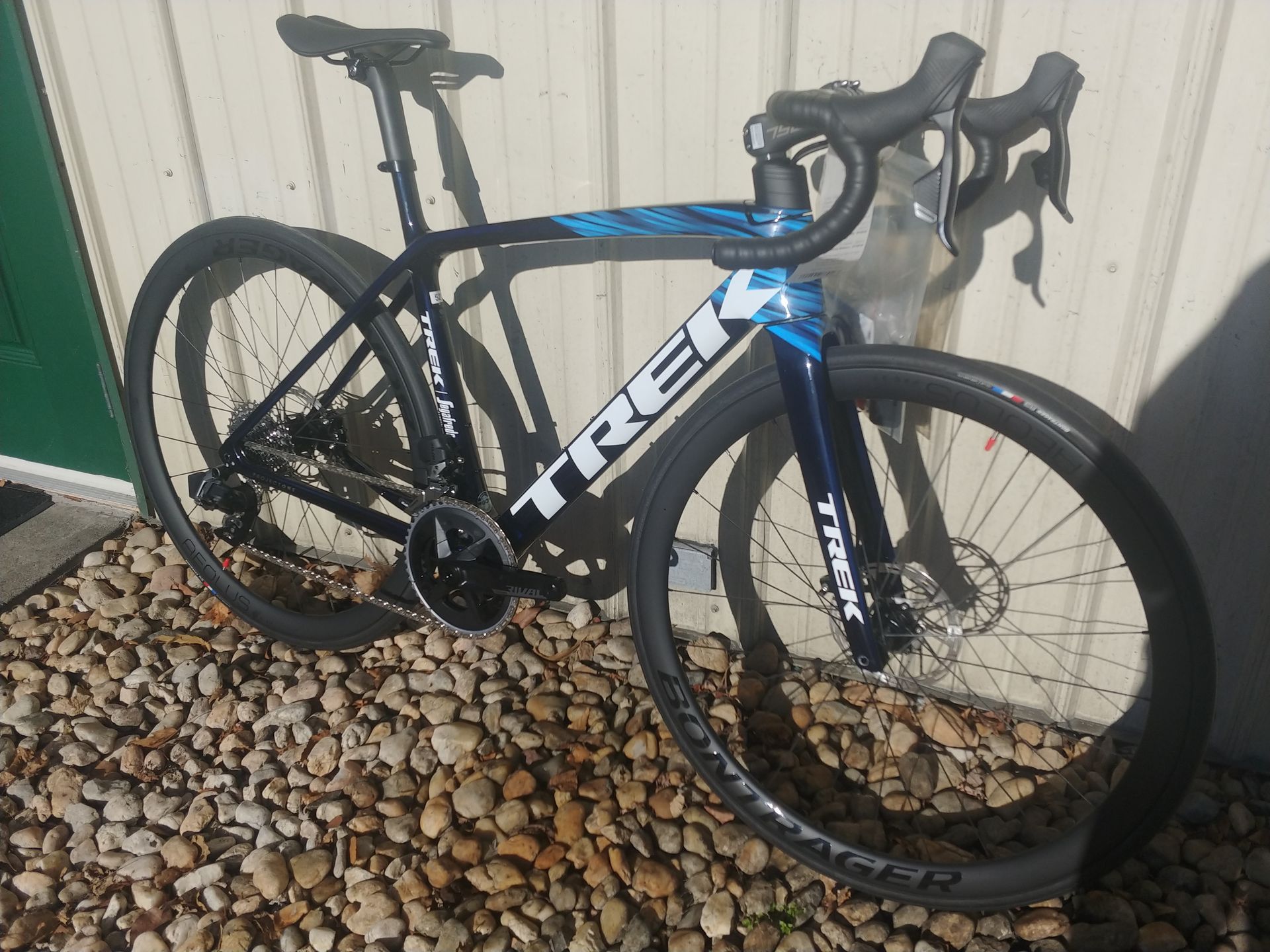Blue Trek road bike parked against a wall on gravel.