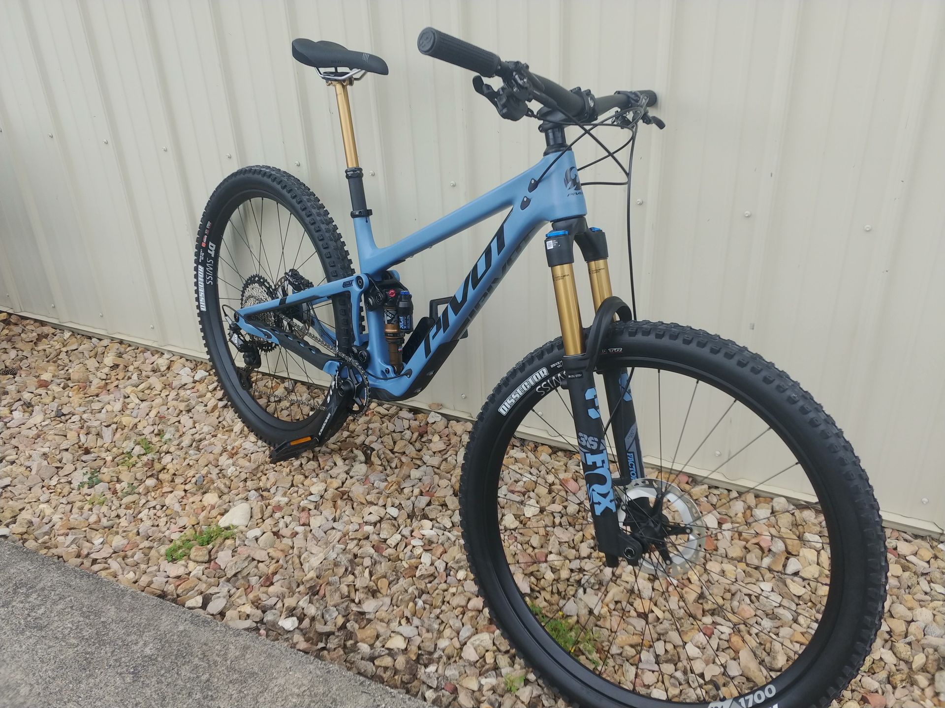 Blue mountain bike parked on gravel beside a corrugated metal wall
