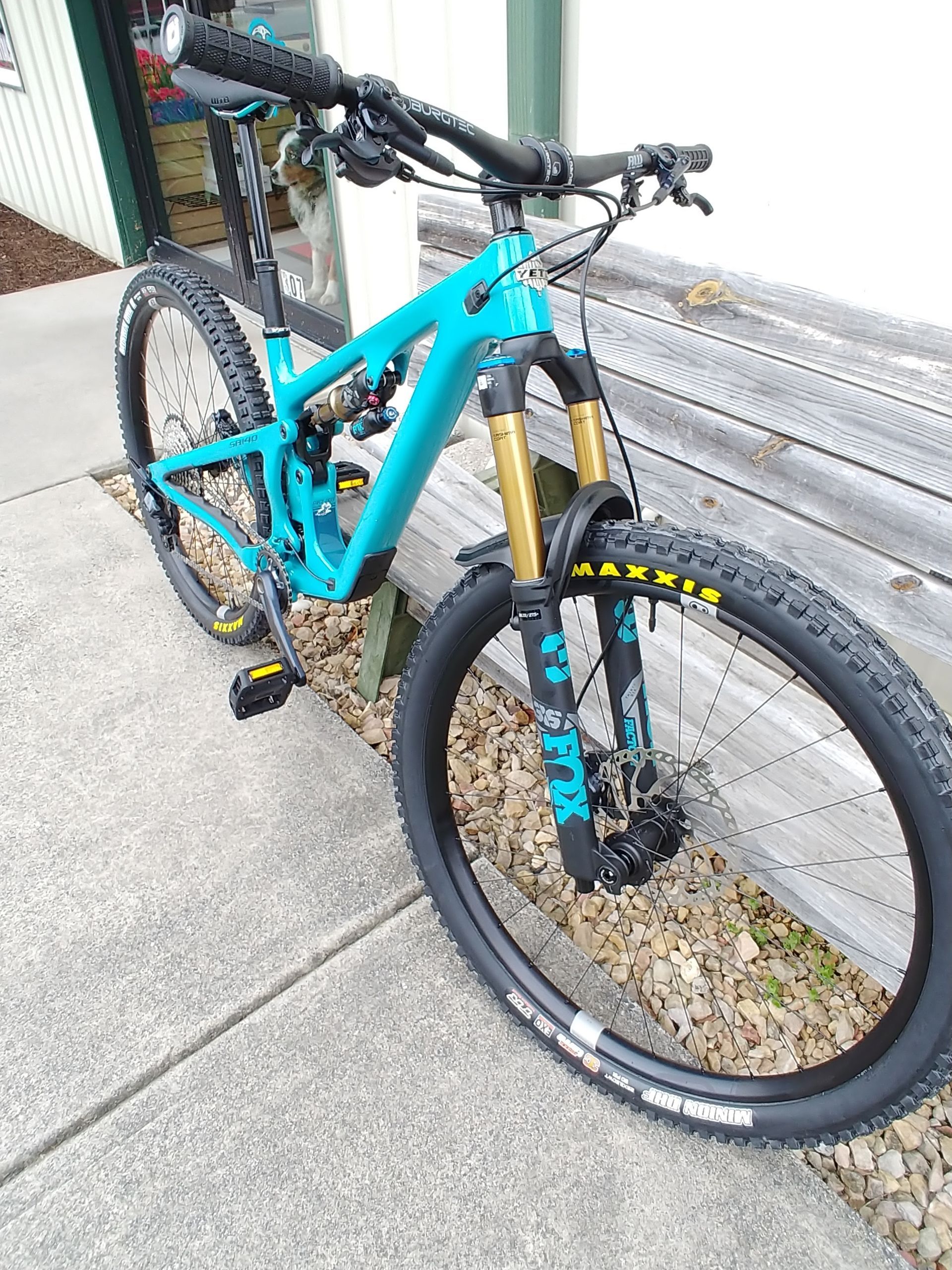 Turquoise mountain bike with black and yellow accents parked on a sidewalk beside a wall