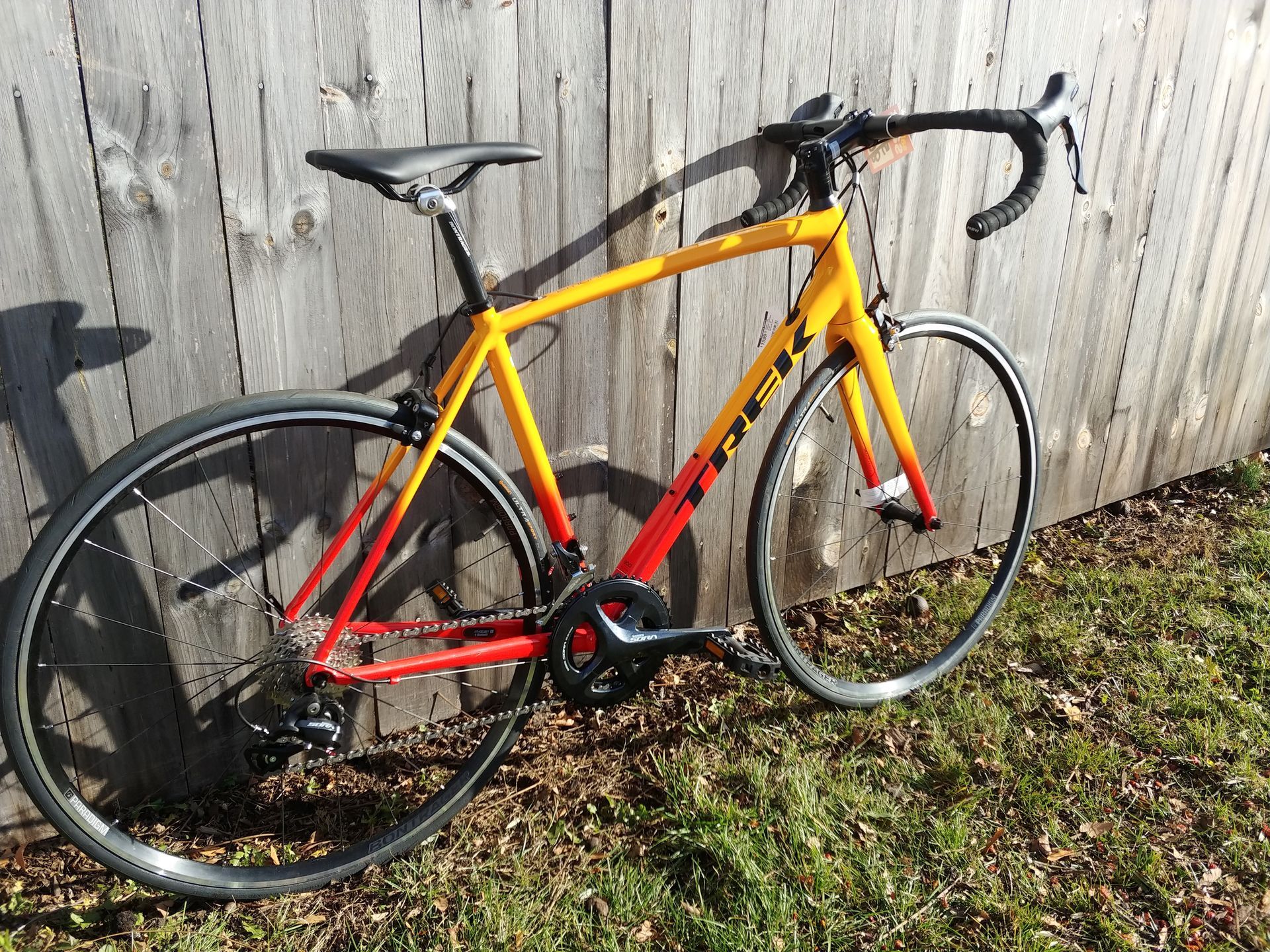 Yellow and red road bike leaning against a wooden fence on grass