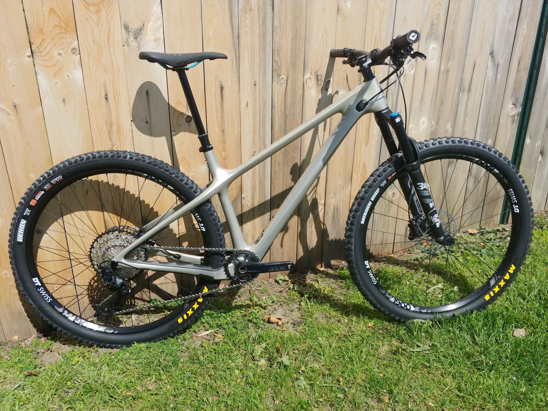 Tan mountain bike parked on grass in front of a wooden fence.