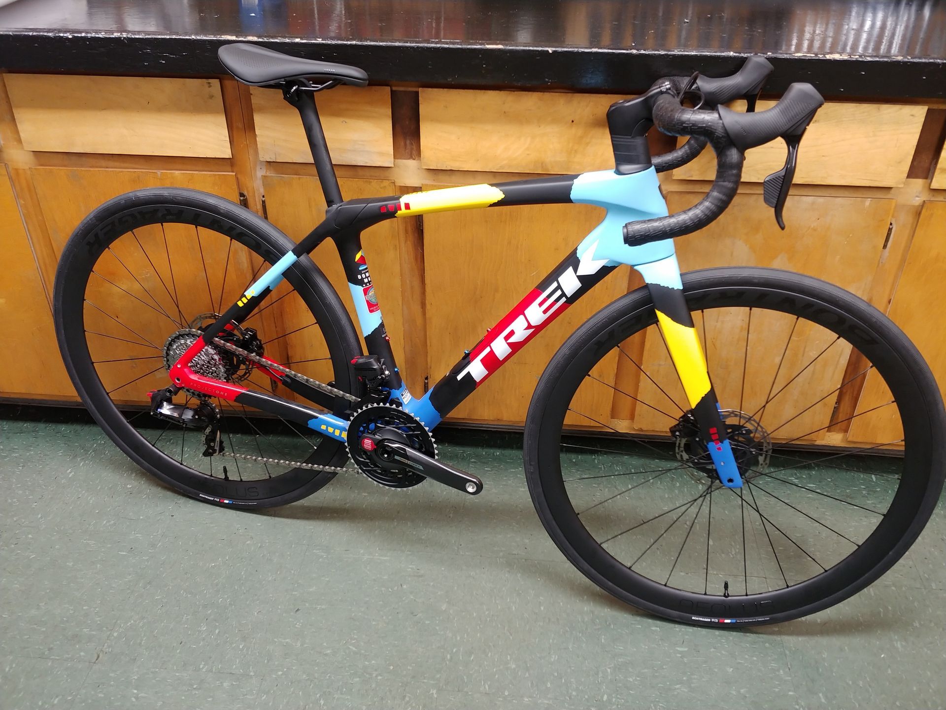 Colorful Trek road bike leaning indoors against a wooden wall.