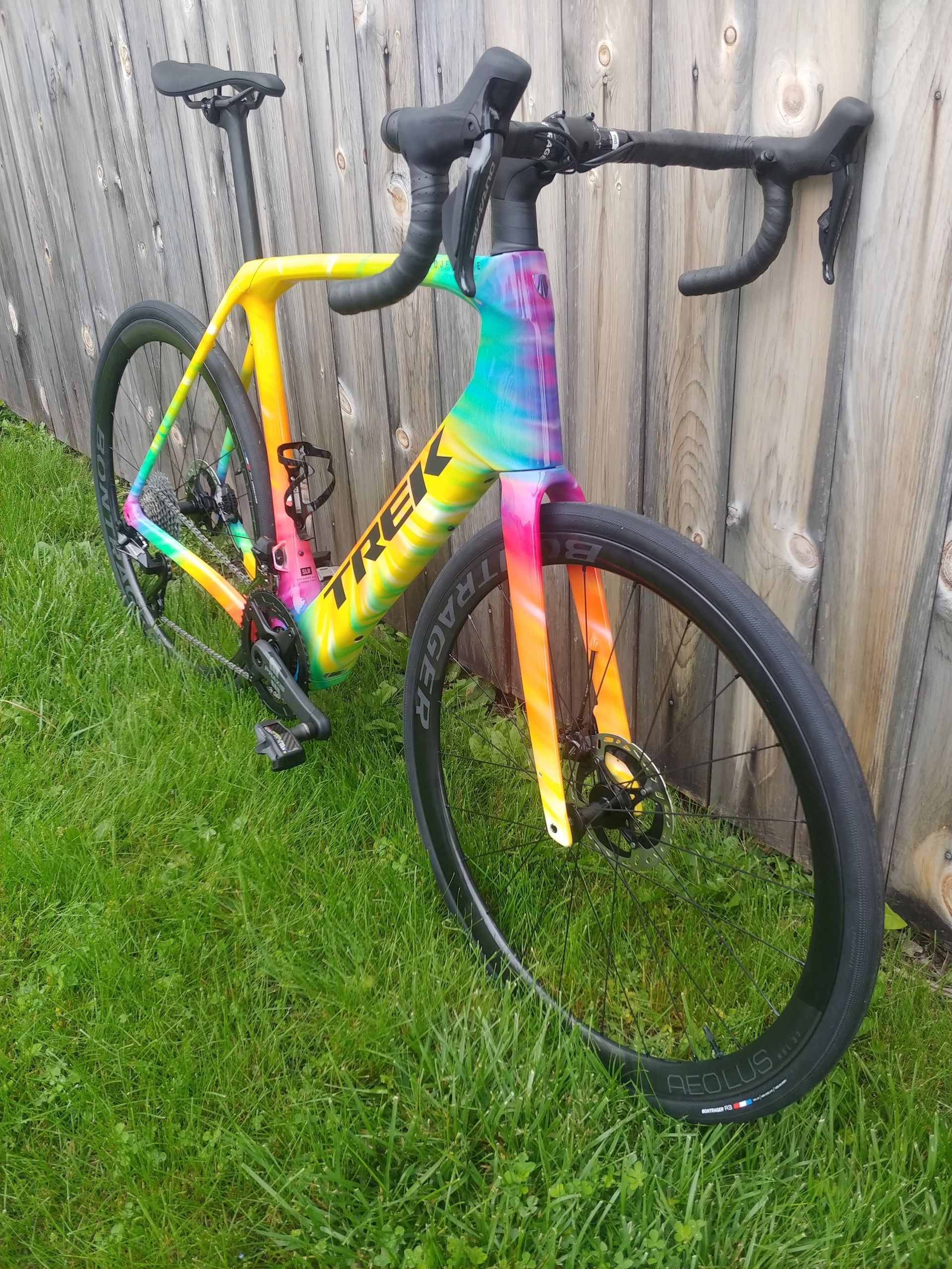 Colorful rainbow-painted road bike leaning against a wooden fence on grass.