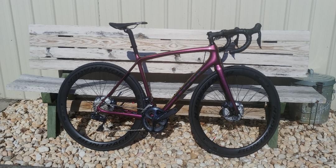 Maroon road bike with black wheels leaning against a weathered white wooden fence outdoors.
