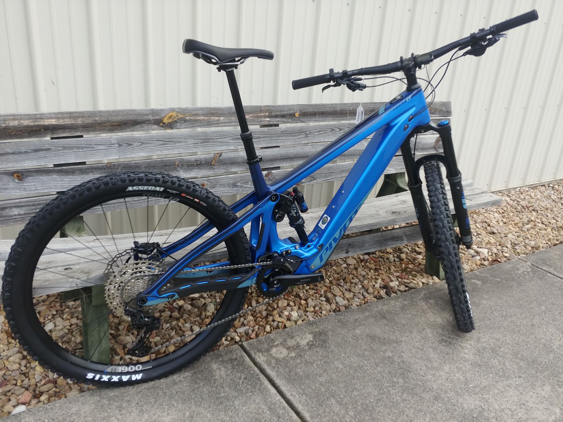Blue mountain bike leaning against a wall on pavement with gravel рядом