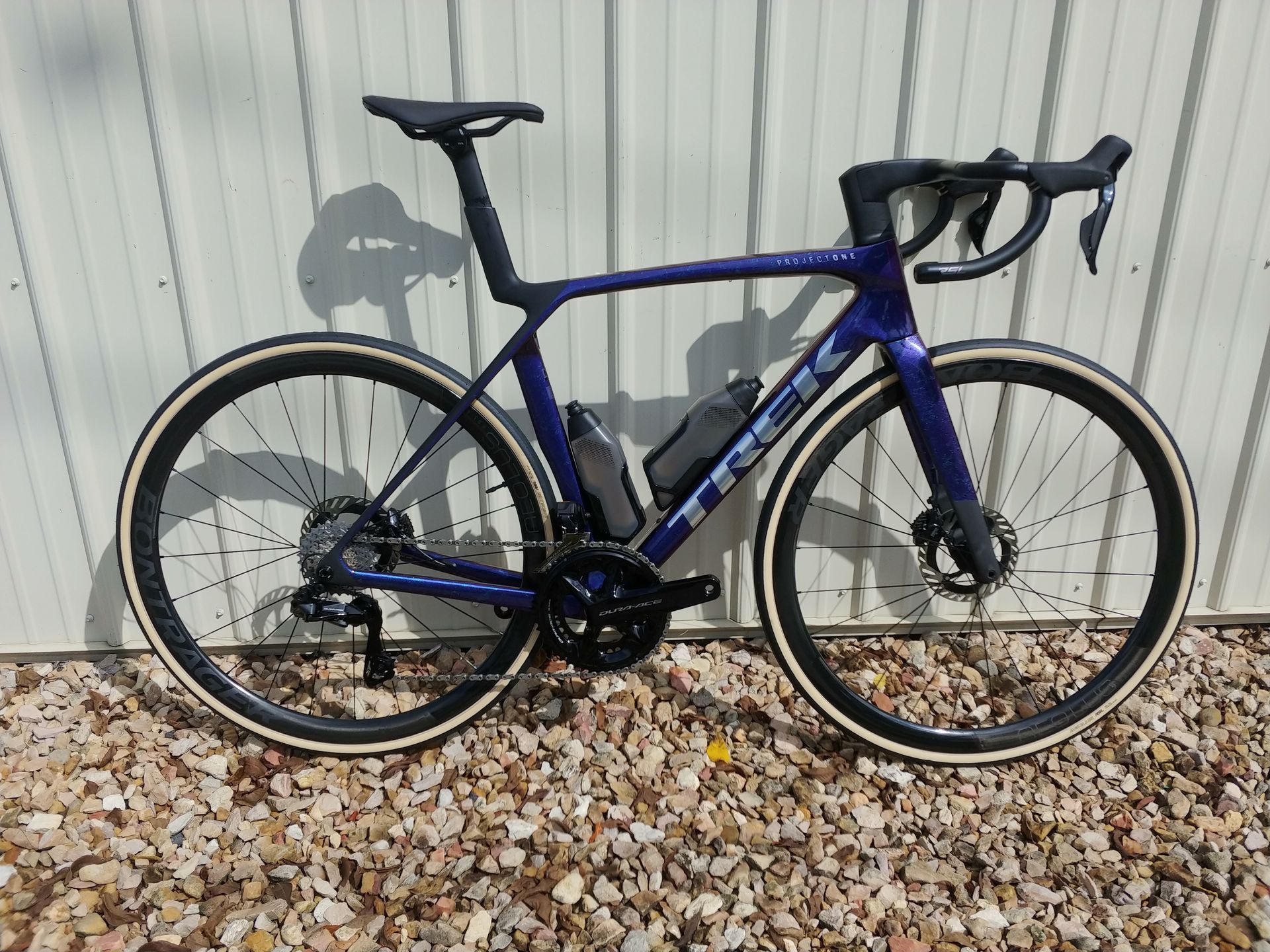 Blue road bike leaning against a corrugated metal wall on gravel.