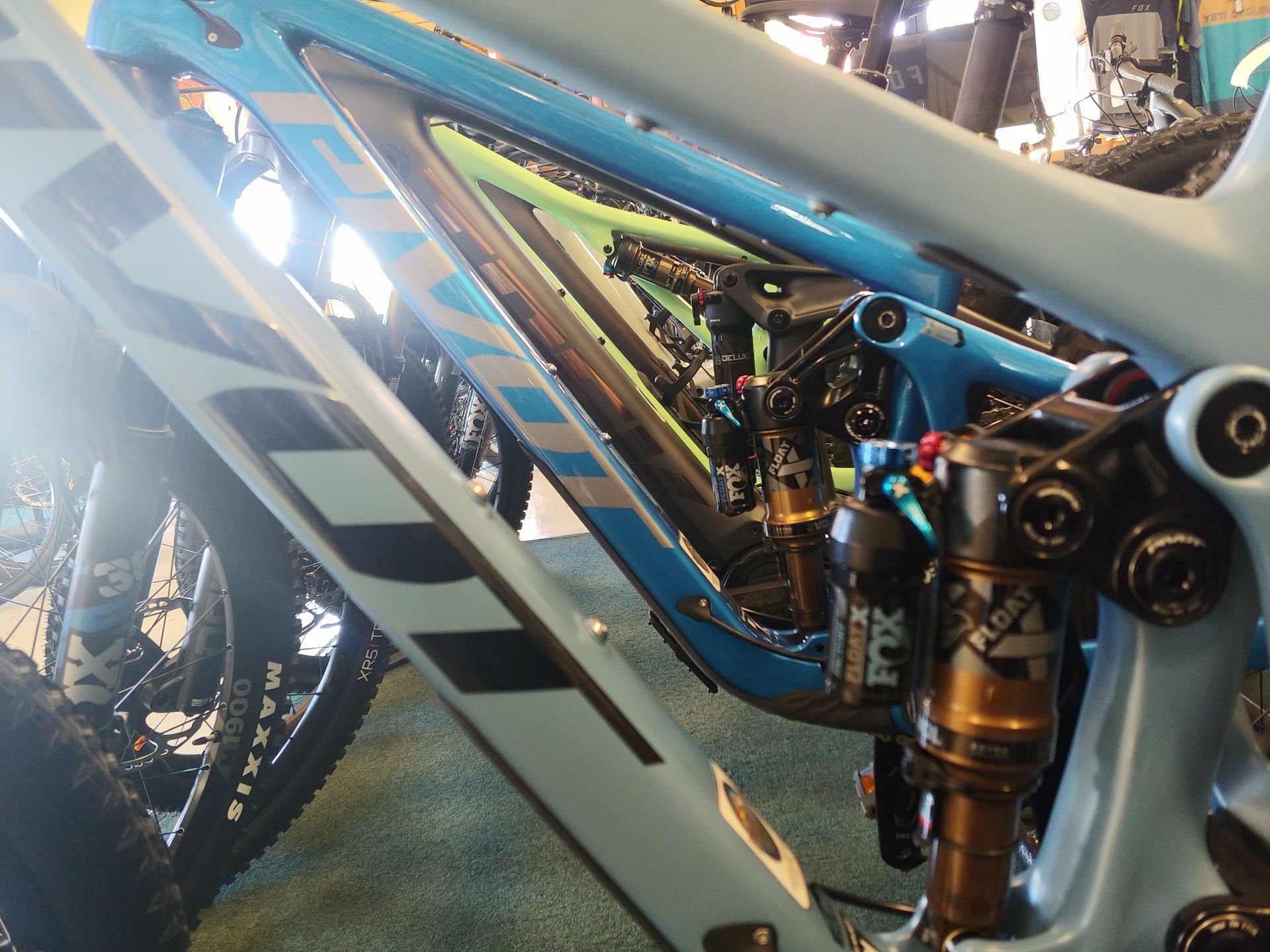 Close-up of a blue mountain bike frame and rear suspension, with wheel and chain visible.