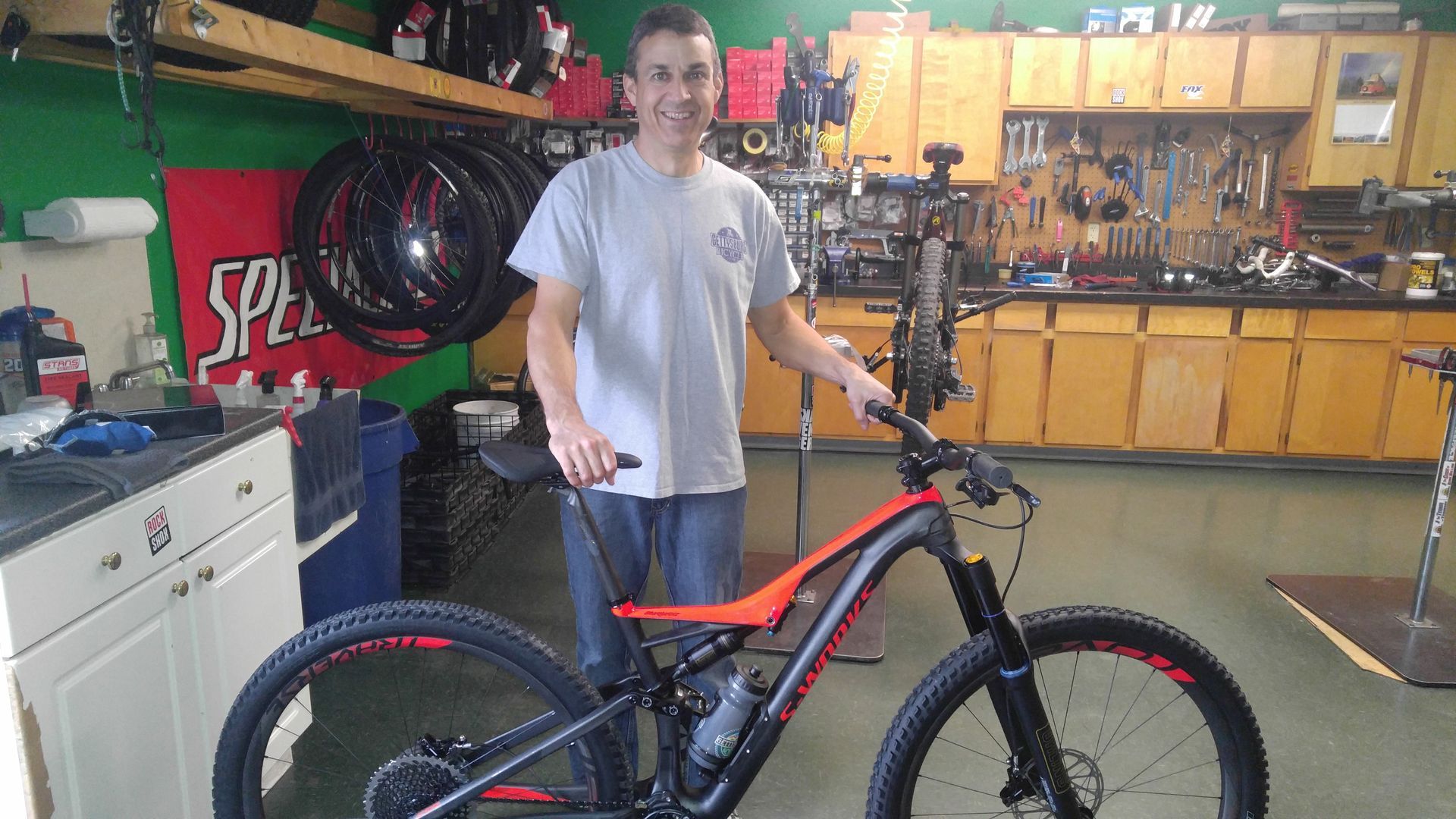 Person standing beside a black-and-red mountain bike in a workshop garage.