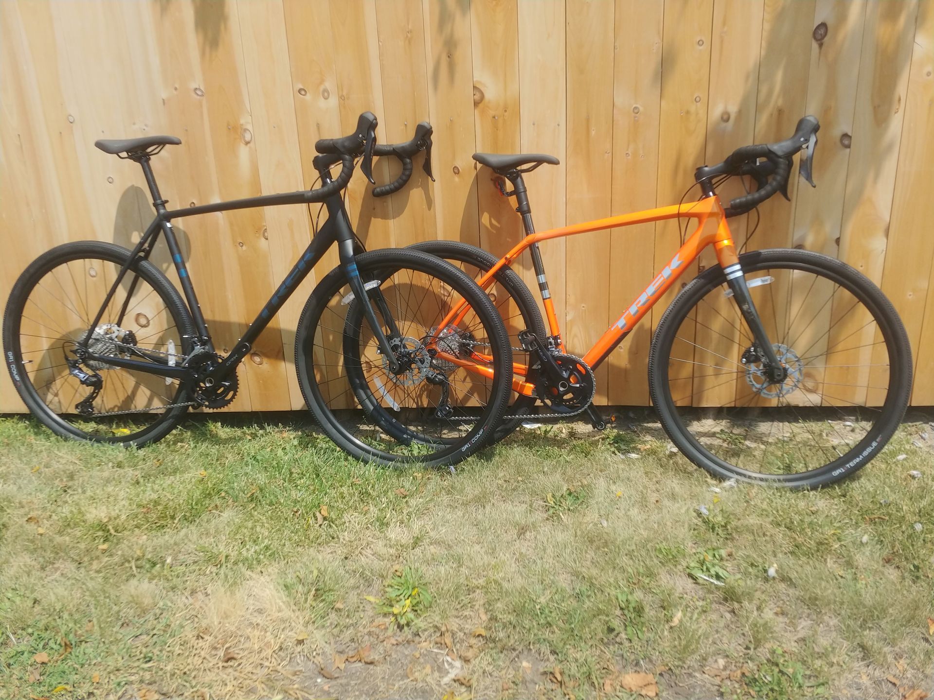 Black and orange road bikes leaning against a wooden fence on grass.