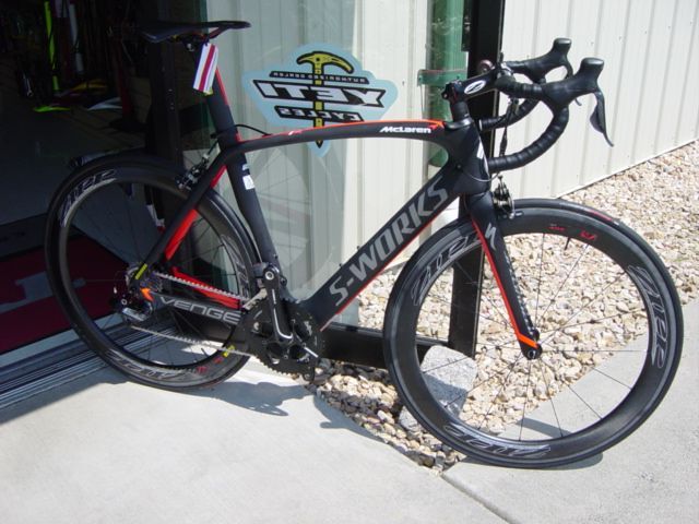 Black and red road bike leaning by a doorway on a concrete patio with gravel beside it