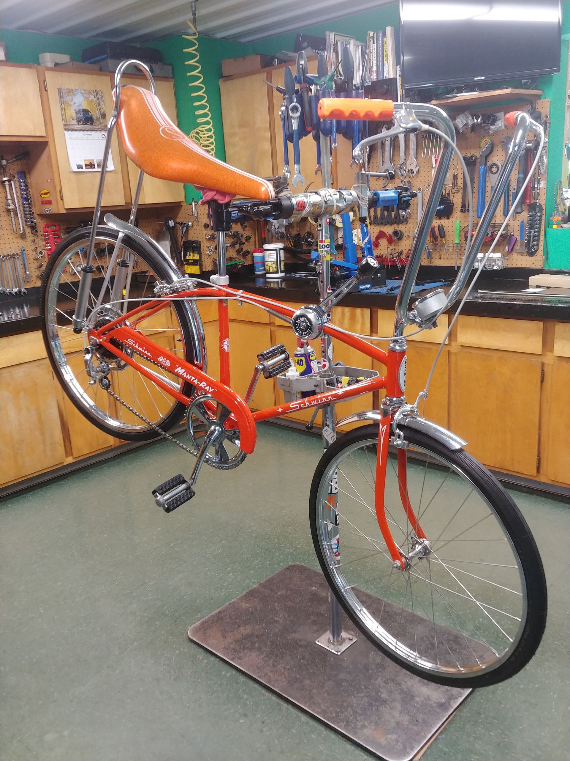 Red recumbent-style bicycle on display in a bike shop, with orange seat and handlebars.