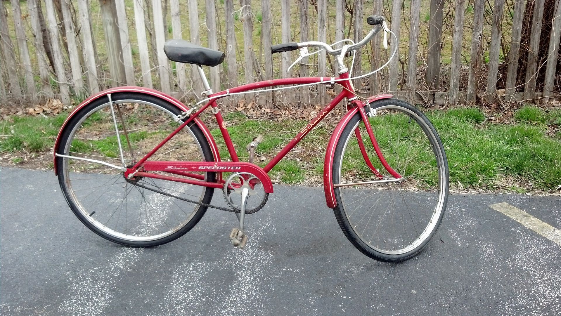 Red vintage bicycle parked on pavement beside a wooden fence and grass.