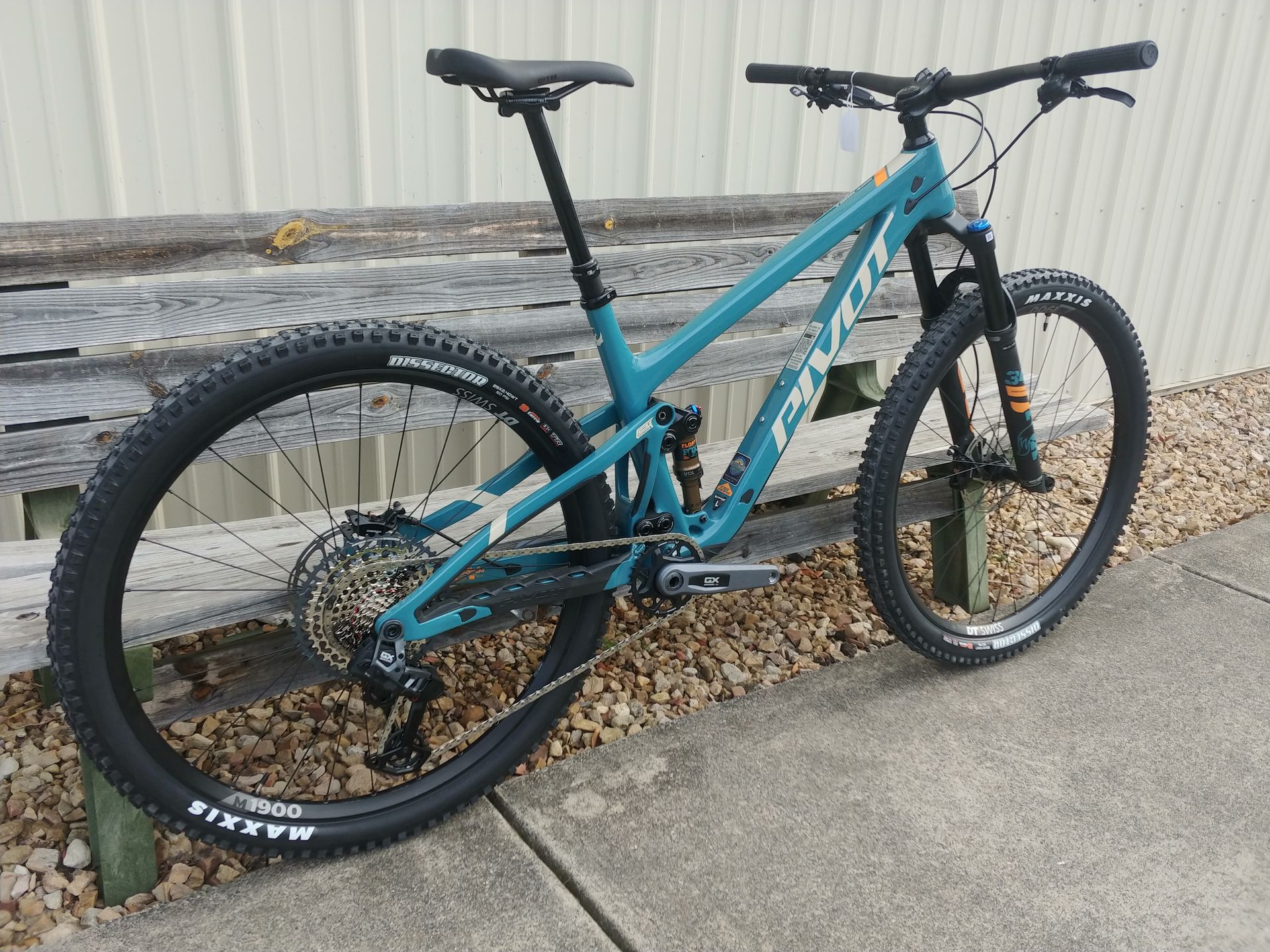 Teal mountain bike with thick tires parked on a concrete path beside a corrugated wall.