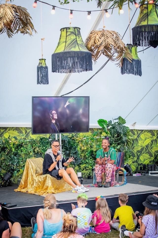 Gok Wan is sitting on a stage talking to a group of people.