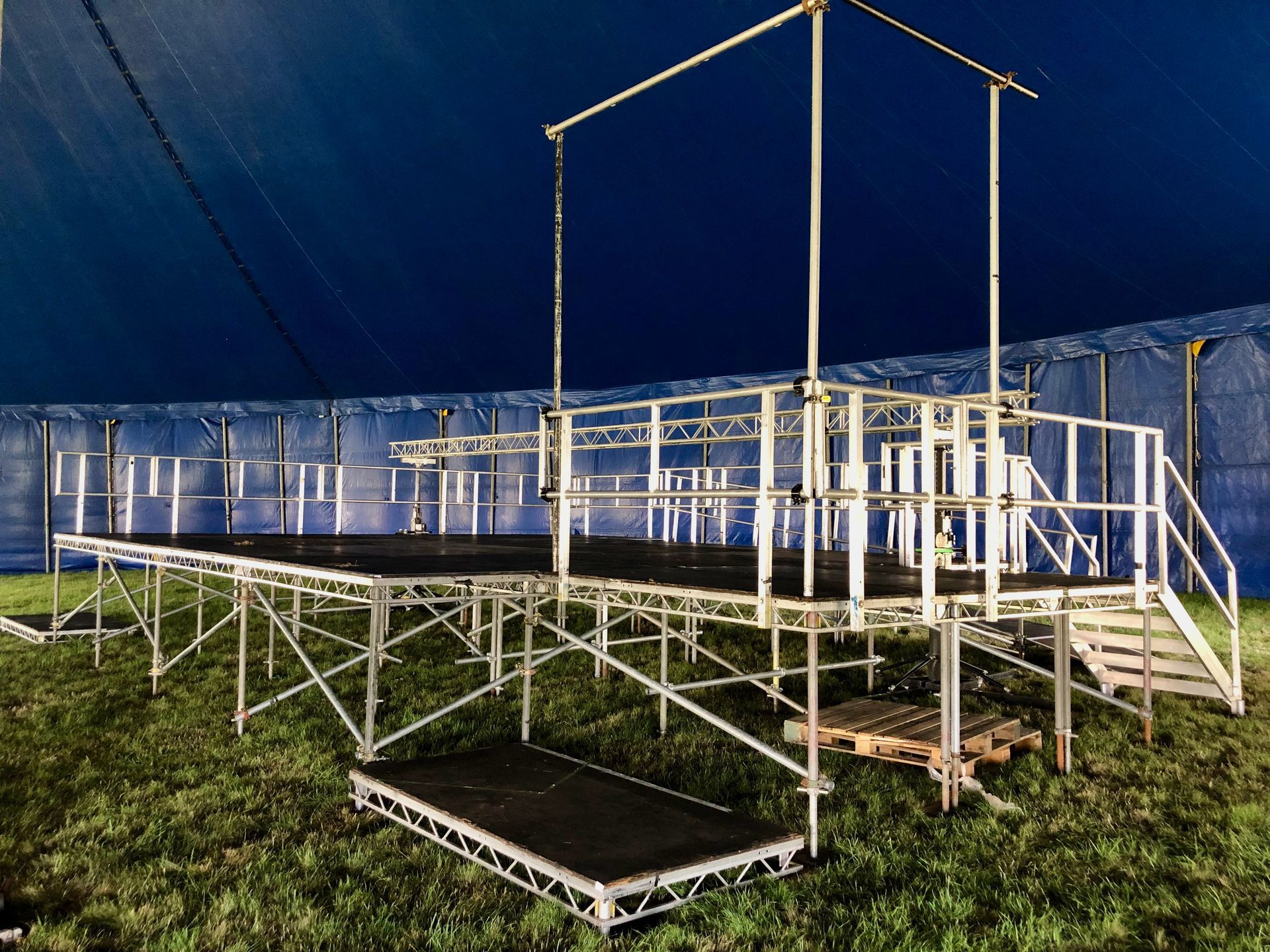 A large stage is positioned in the grass in front of a sports pitch