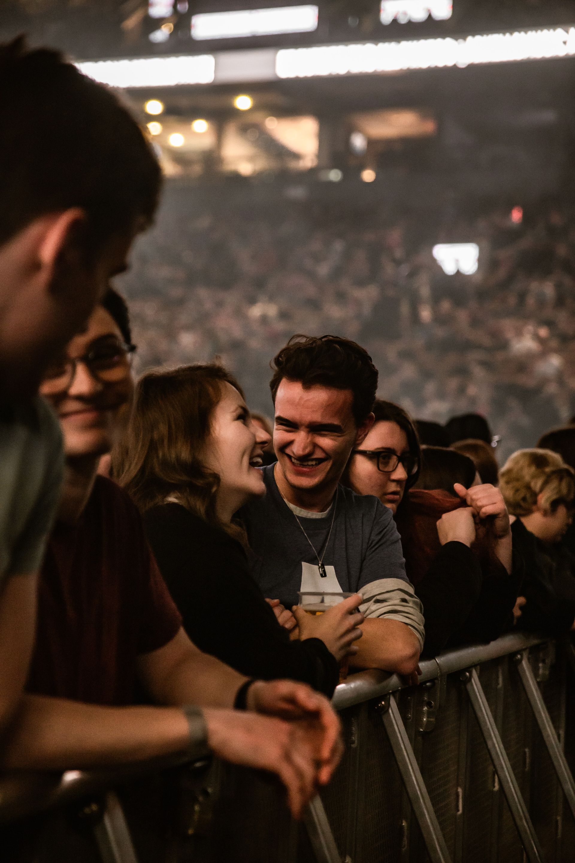 A group of people are stansing in a stadium in front of crowd barriers watching a concert.