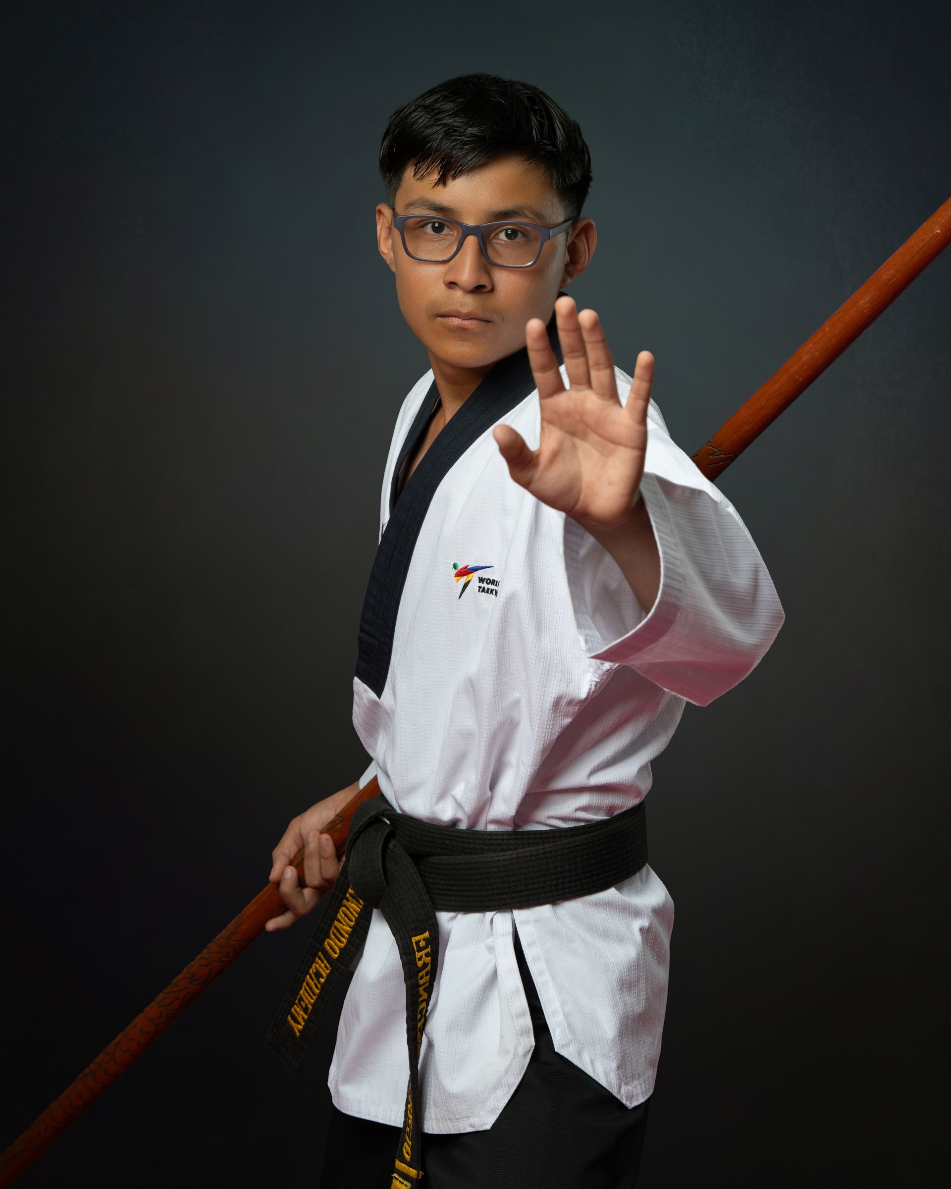A group of six martial artists in uniforms and one in a suit stand posing for a photo in a taekwondo studio.