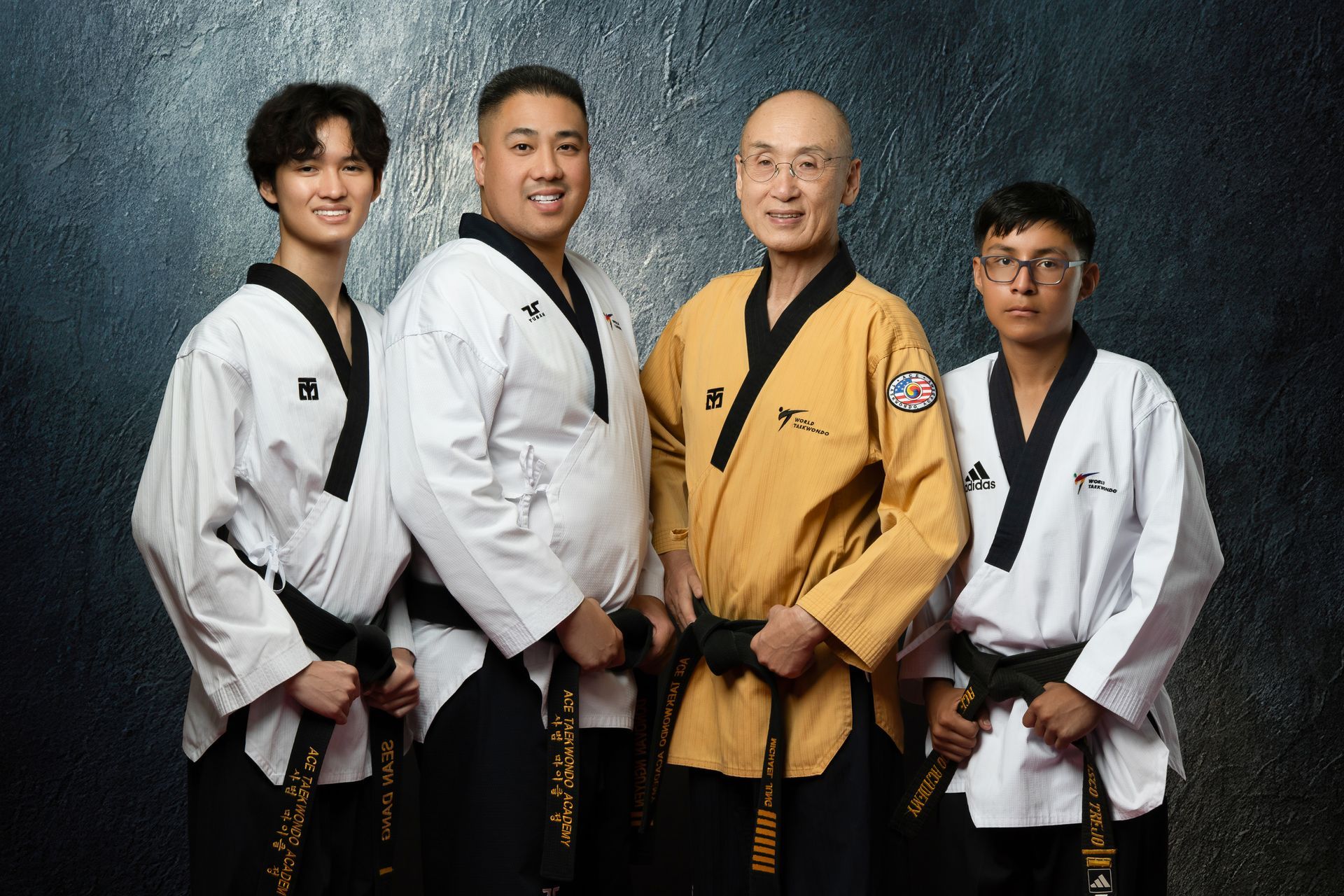 Two people in martial arts uniforms stand before American and South Korean flags; one holds a gold trophy.