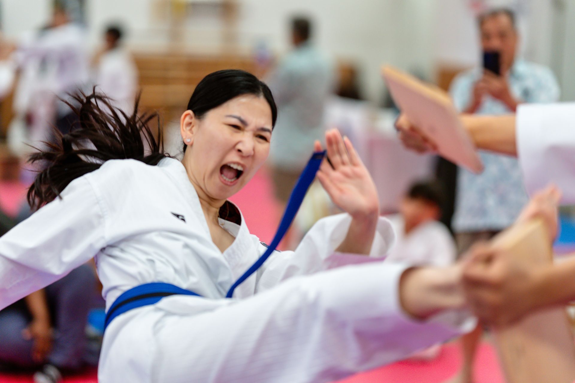 A person in a white uniform holding a wooden board for another person to practice a kick during a martial arts class.