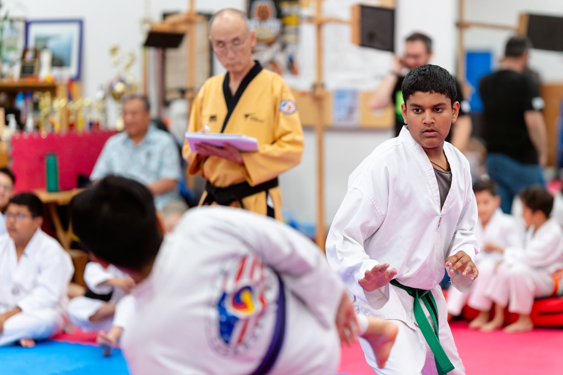 Four people stand in a martial arts studio; one person in a black uniform holds a framed certificate.