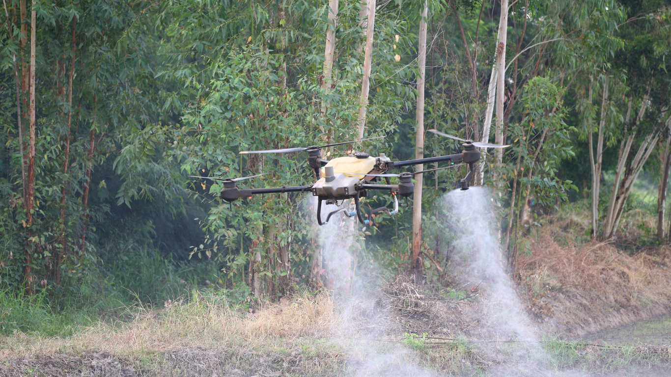 Agricultural drone spraying a field with the forest in the background.