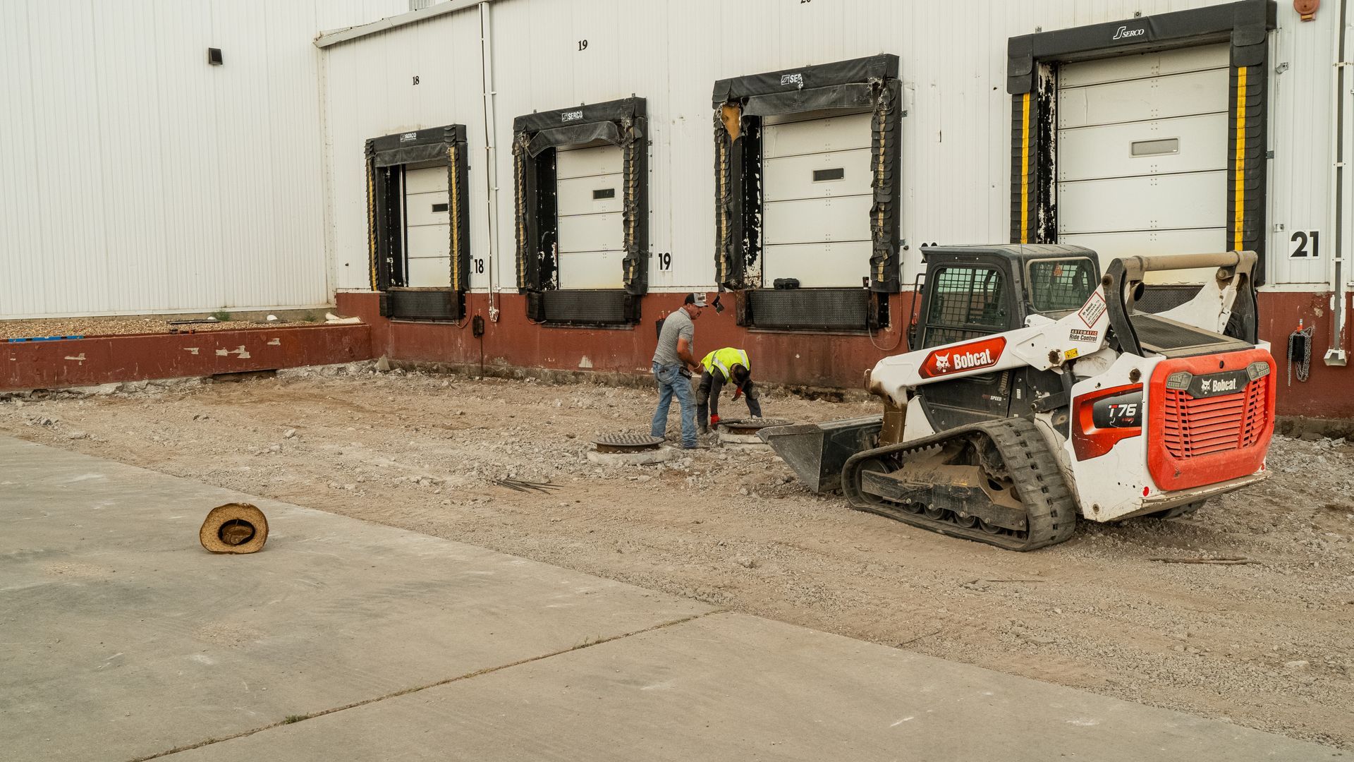 Worker operating a skid steer near loading dock doors at a warehouse