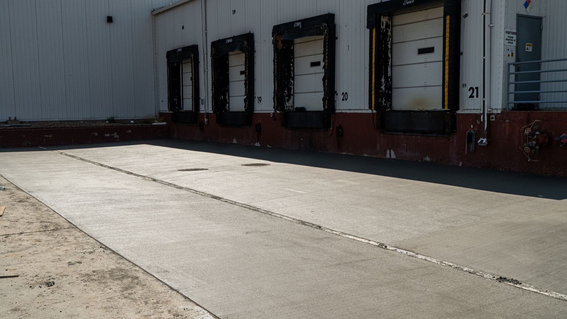 Loading dock with several black dock doors on a white warehouse wall beside an empty concrete lot