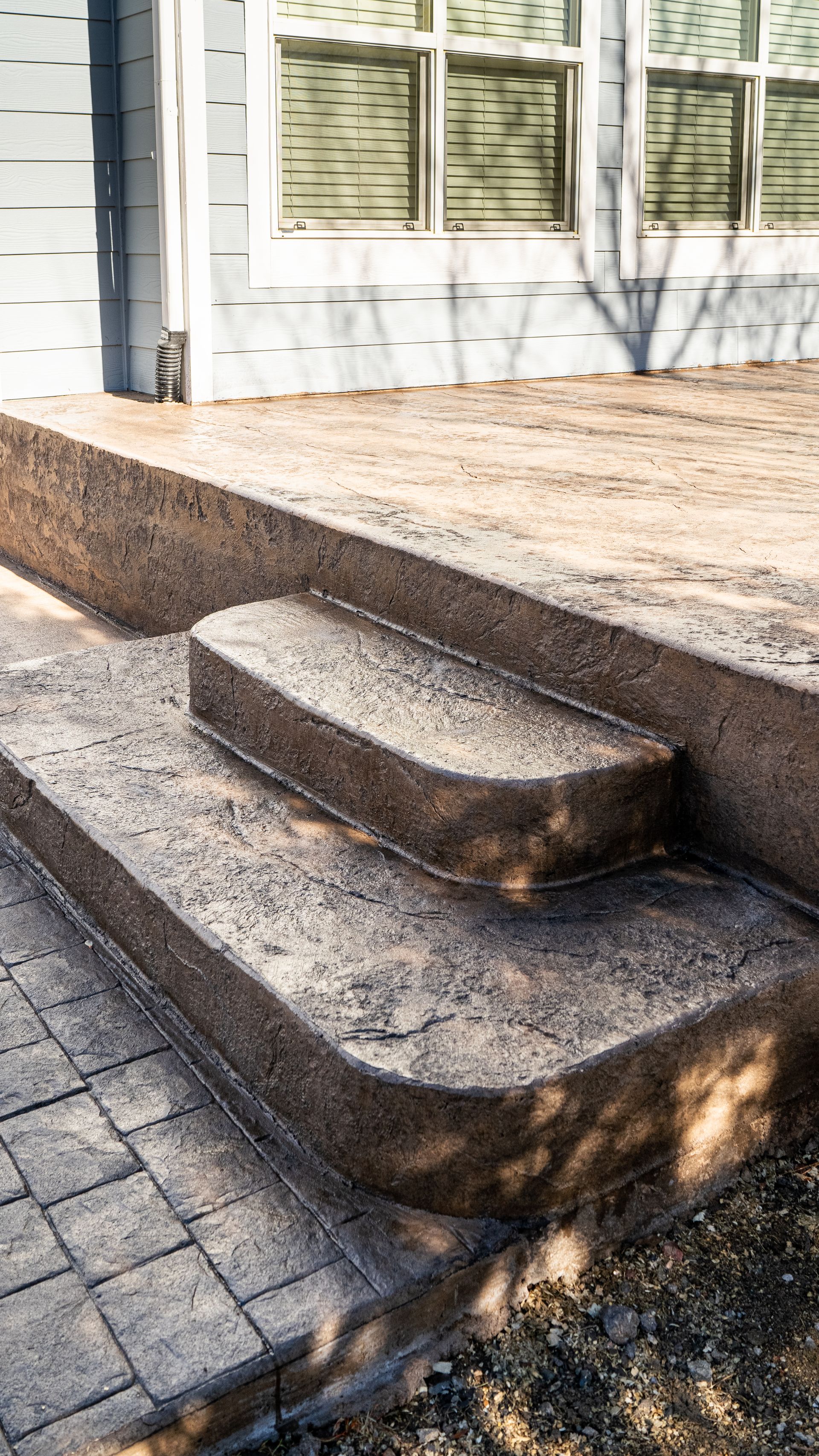 Stone steps leading to a raised patio beside a house with white siding and green shutters