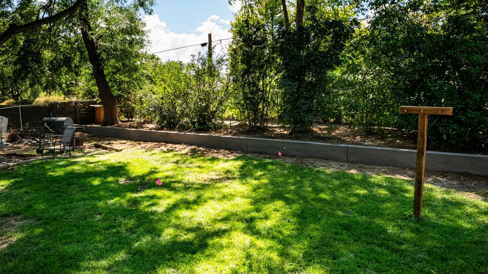 Sunny garden with green lawn, shaded trees, stone path, and wooden signpost by a fence