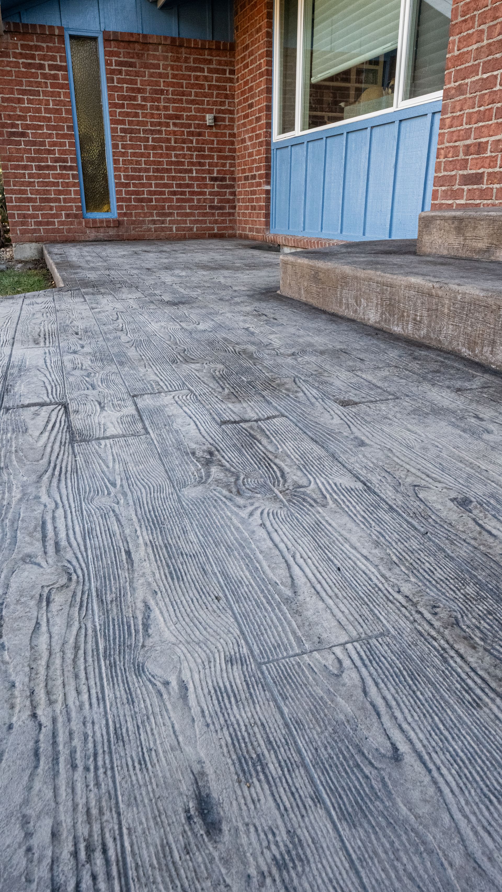 Concrete patio beside a brick house, with steps and a blue fence or railing.