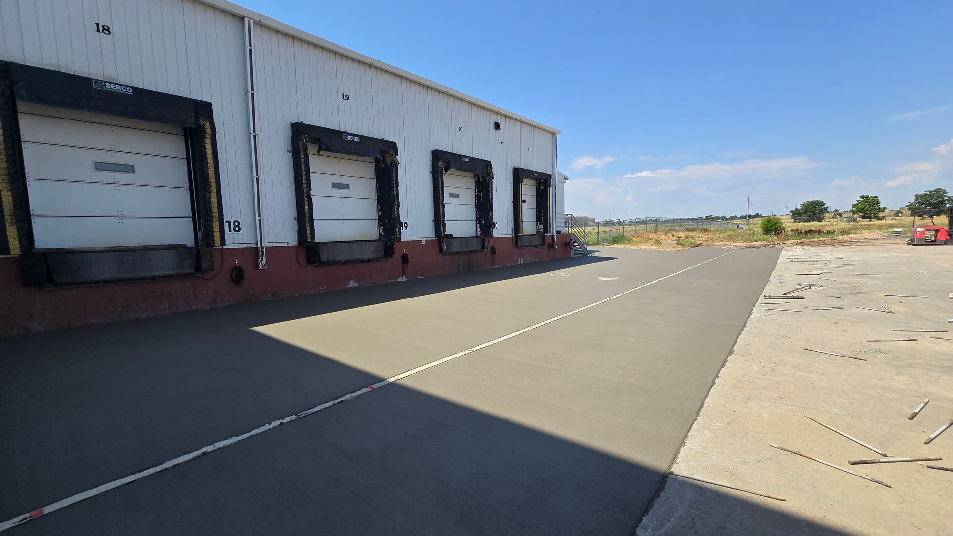 Warehouse loading dock with closed bay doors and a wide empty concrete lot under a clear sky