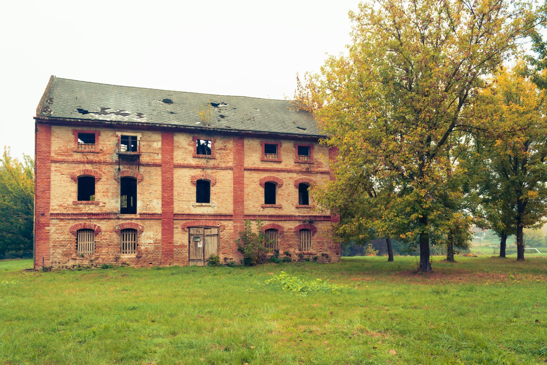 An old brick building is sitting in the middle of a grassy field.