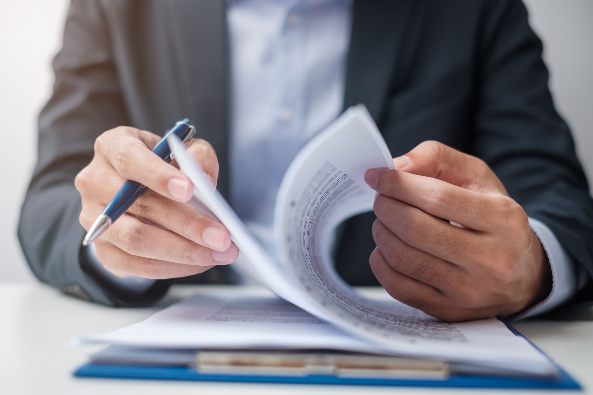 Hands flipping through a document while holding a pen over a blue folder