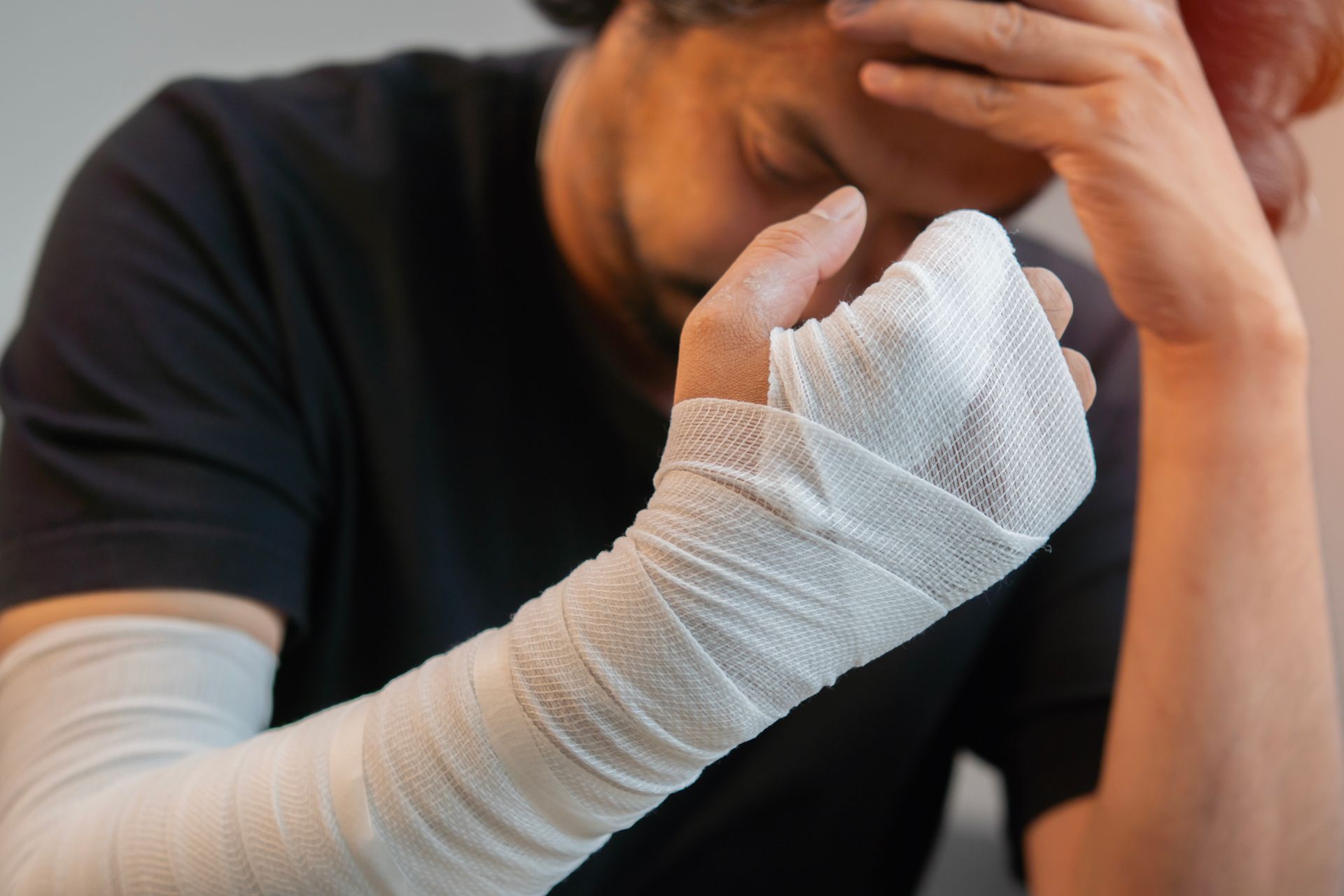 Person with a bandaged hand and wrist resting their face, suggesting injury or pain