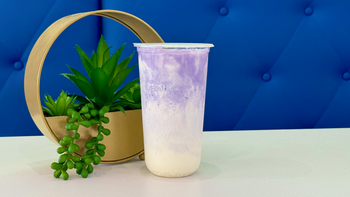 Iced tea in a clear cup beside a gold hoop and green plant on a blue backdrop