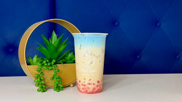 Tall pastel pink drink with blue foam beside a green plant and wooden hoop on a blue backdrop
