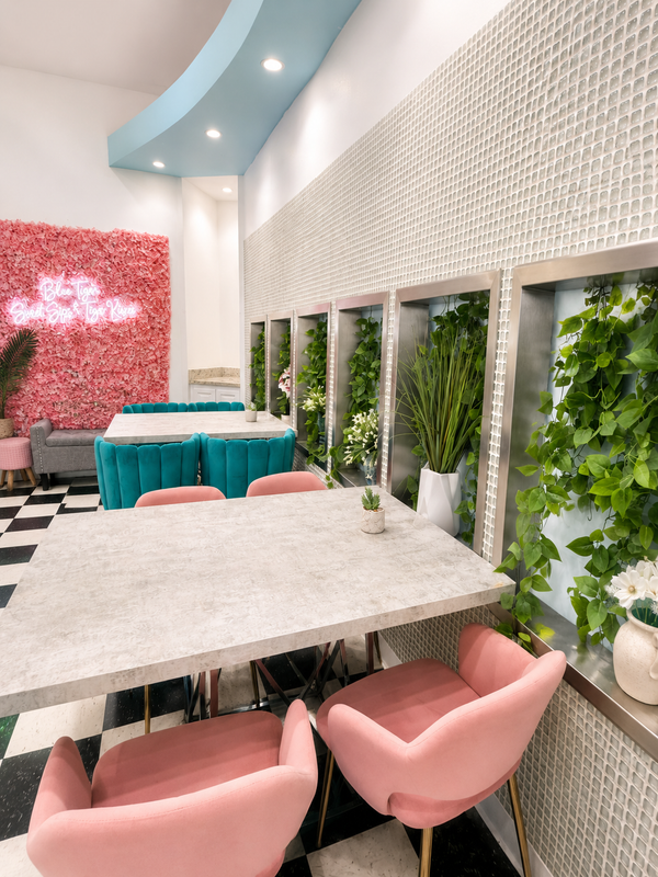 Stylish café interior with pink chairs, turquoise table, white decor, and green wall planters.