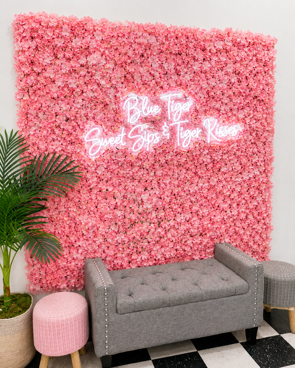 Pink flower wall with neon sign above a gray bench and stool in a decorated interior.