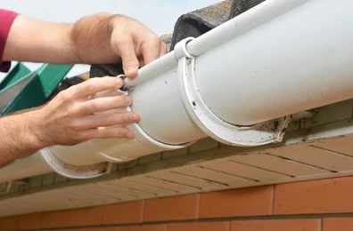 Person installing white gutter on brick building.