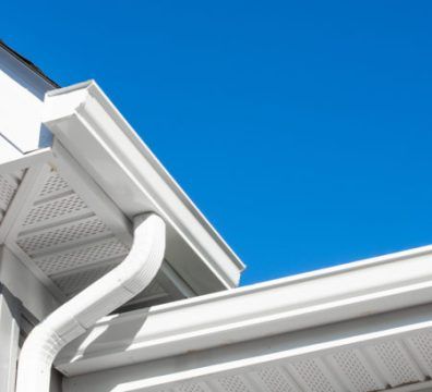 White rain gutters and downspout on a house against a bright blue sky.
