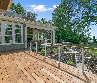 Wooden deck with railing, house, and landscaped yard. Blue sky, green trees.