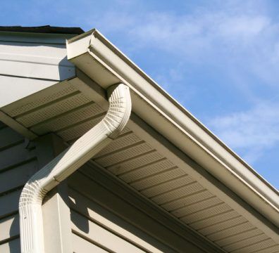 White gutter system on a light-colored house with a blue sky background.